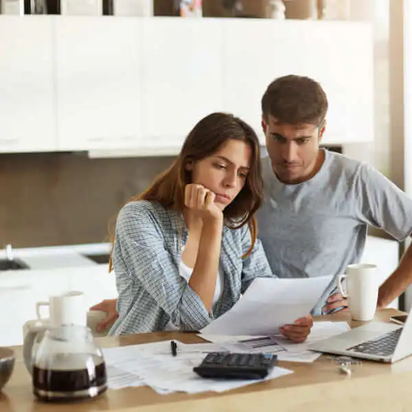 Un jeune couple assis à la table de leur cuisine, l'air inquiet en examinant des factures financières pour déterminer s'ils peuvent obtenir un prêt instantané au Canada.