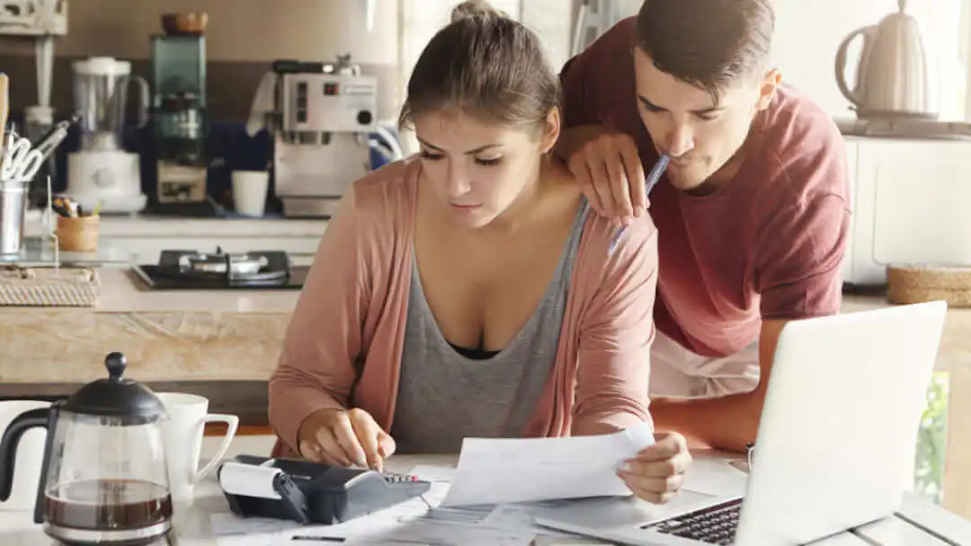 Une personne heureuse tenant un smartphone et une carte de crédit, assise devant un ordinateur portable avec des sacs de courses à proximité, illustrant les solutions d'argent rapide en ligne au Canada.