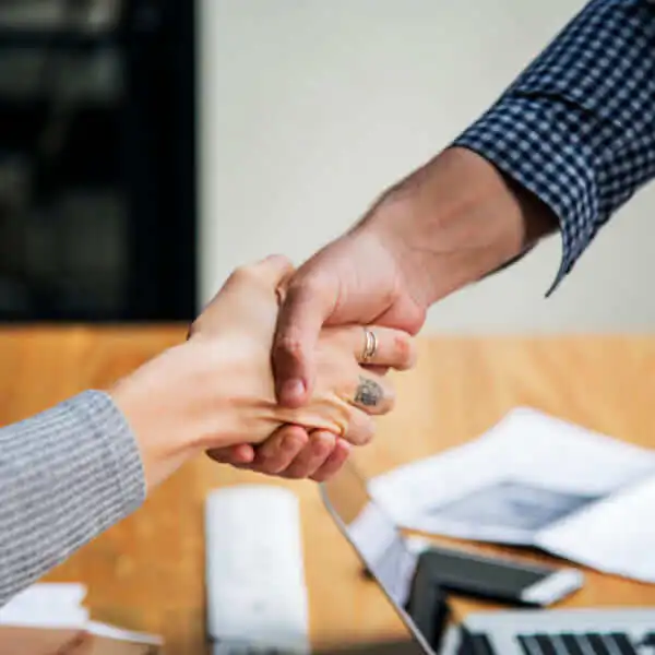 Gros plan d'une poignée de main ferme au-dessus d'un bureau avec un ordinateur portable, symbolisant un accord réussi avant une demande de prêt.