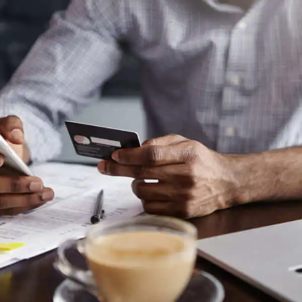 A person holding a credit card and using a smartphone to manage finances and improve their credit score over the long term.