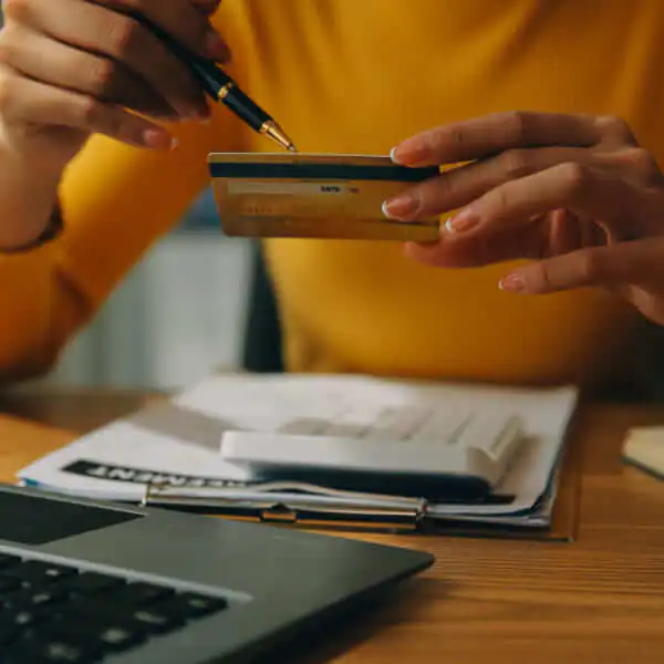 A person holding a credit card while reviewing financial documents and using a calculator to improve their debt-to-income ratio.